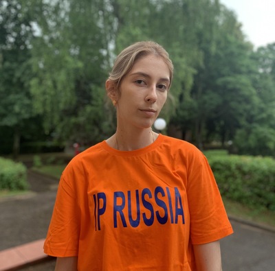 Участник языкового лагеря IP Russia в фирменной оранжевой футболке на фоне зелёного пейзажа.
